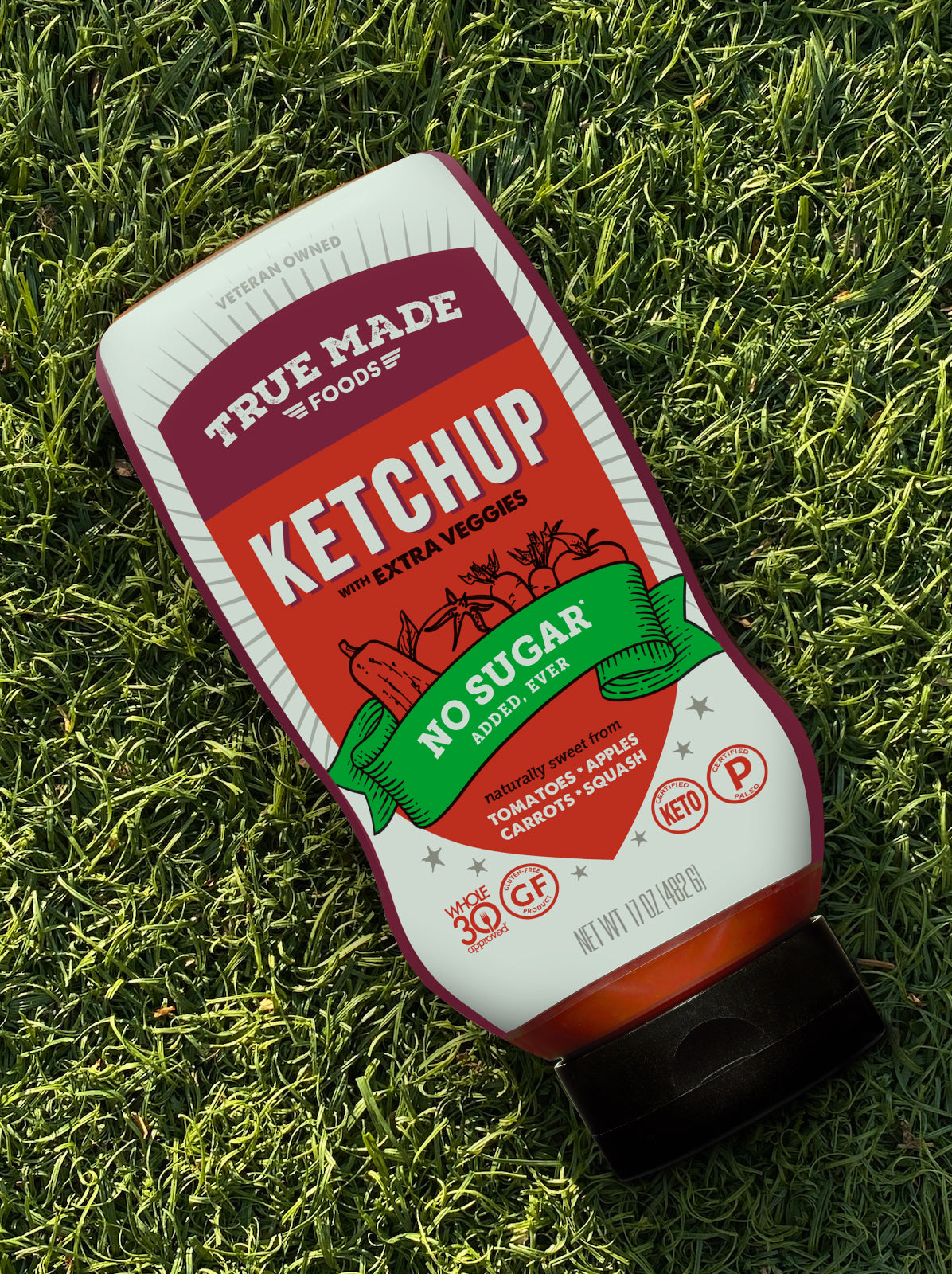 A bottle of True Made Foods no-sugar ketchup placed on green grass.