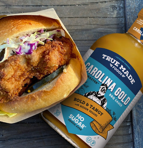 Carolina Gold BBQ sauce bottle beside a crispy chicken burger with slaw, ideal for healthy July 4th grilling.