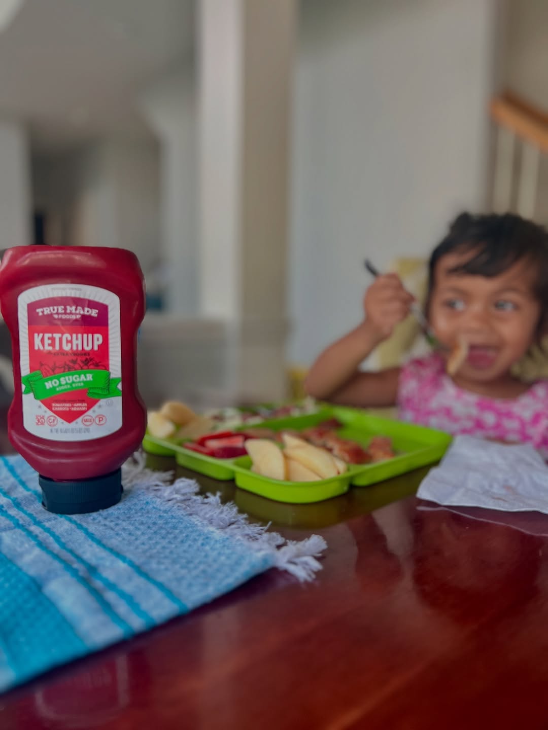 Child enjoying a meal with apple slices, fries, and True Made Foods ketchup on the table.
