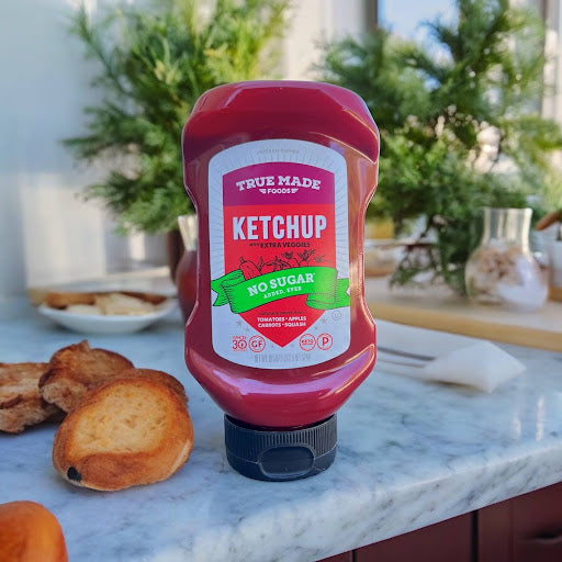 A bottle of True Made Foods Ketchup on a white-covered table.