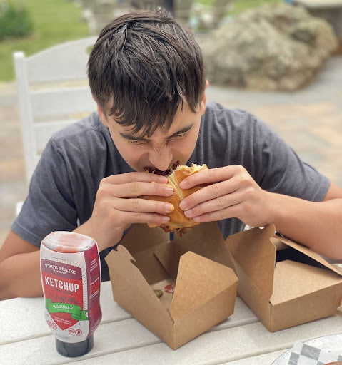 A boy enjoying a burger topped with True Made Foods' No Sugar Ketchup.