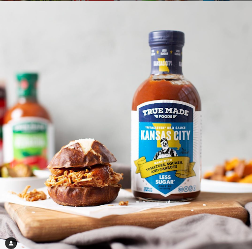 A burger served with True Made Foods Kansas City BBQ sauce bottle.