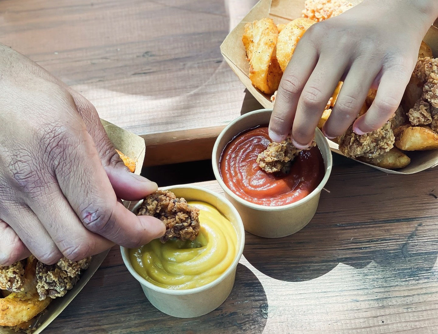  Two people dipping chicken sides in True Made Foods Ketchup and Mustard.