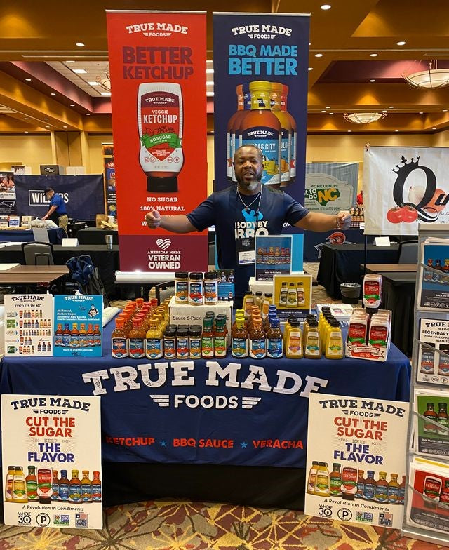 A smiling pitmaster displaying True Made Foods’ products at a trade show.