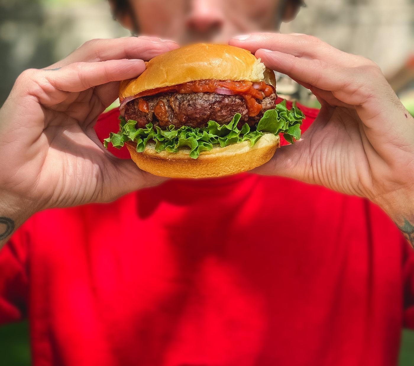 Man in a red T-shirt holding a saucy burger made with True Made Foods, smiling before a bite.