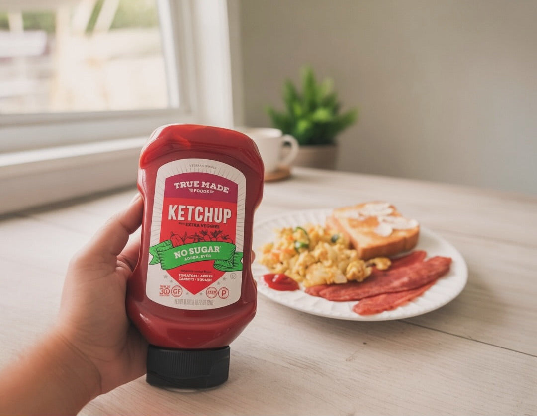 Healthy breakfast plate with scrambled eggs, toast, and bacon beside a bottle of True Made Foods no-sugar ketchup.