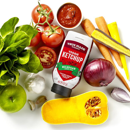 True Made Foods’ no-sugar veggie ketchup surrounded by tomatoes, squash, onions, spinach, and other natural ingredients.