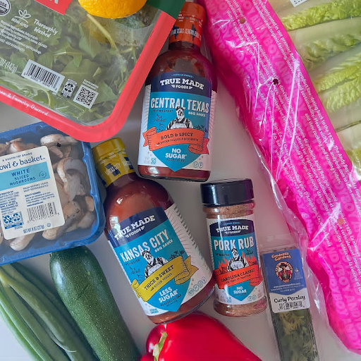 True Made Foods BBQ sauces, rubs, mushrooms, vegetables, and herbs arranged on a flat surface.