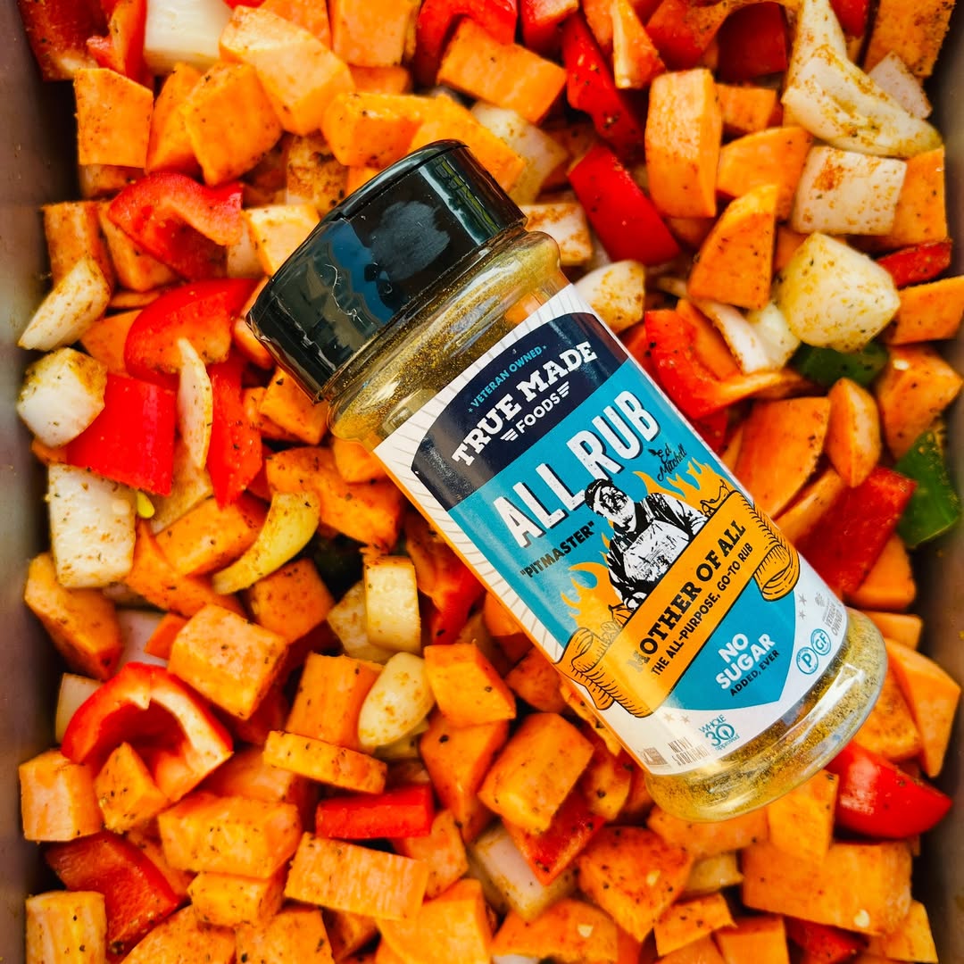 True Made Foods All Rub seasoning bottle on chopped sweet potatoes and bell peppers.