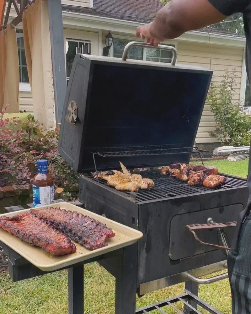Person opening a smoker grill filled with racks of ribs and chicken wings glazed with True Made Foods BBQ Sauce.
