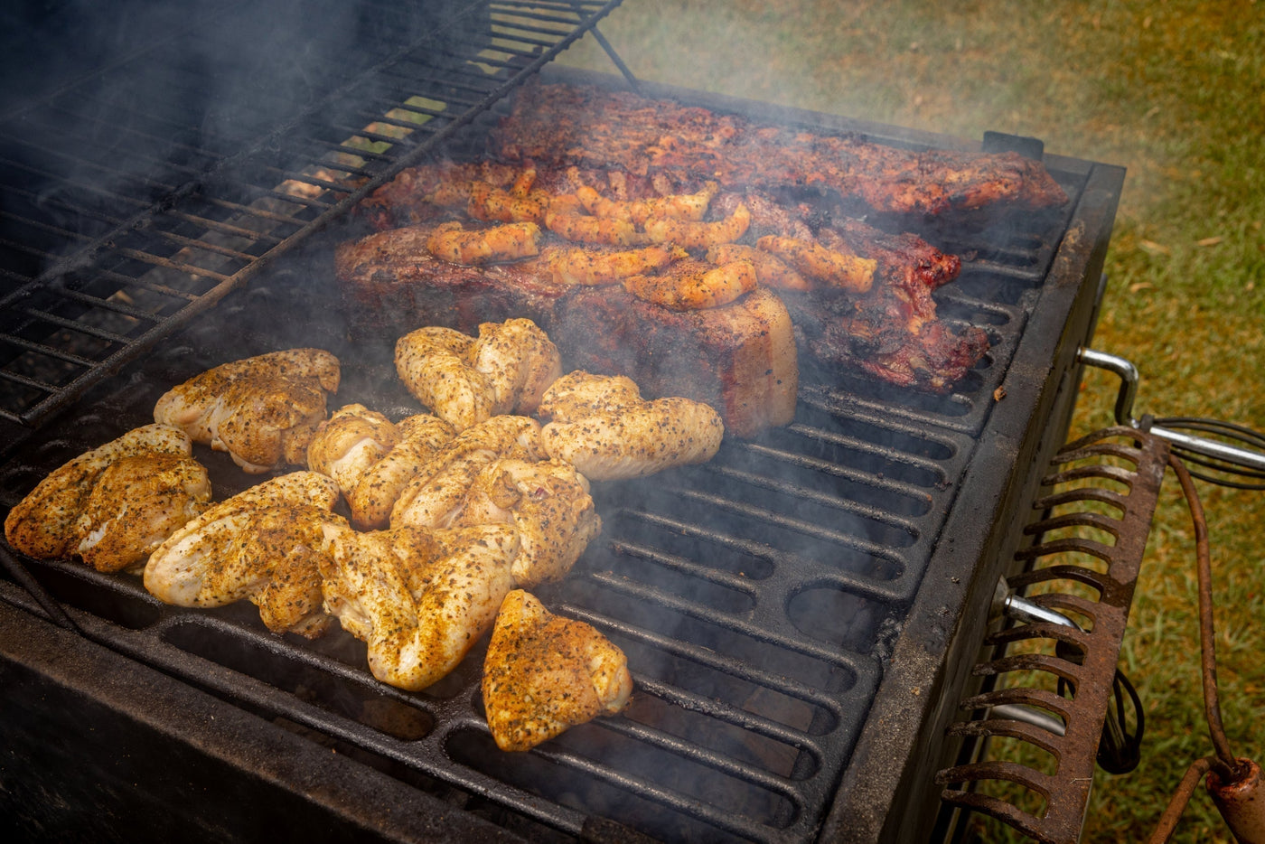 A smoky backyard BBQ grill loaded with chicken, sausages, and ribs sizzling over hot coals using True Made Foods’ rubs.