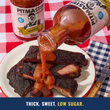 Load image into Gallery viewer, A bottle of Pitmaster BBQ Sauce is tilted over a plate of smoked ribs, pouring the thick red sauce. Another bottle of Pitmaster Original BBQ Sauce sits in the background on a red-and-white checkered tablecloth with a fork nearby.
