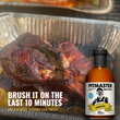 Load image into Gallery viewer, A bottle of Pitmaster BBQ Sauce placed beside a cooked piece of meat in a foil pan, with promotional text reading 'BRUSH IT ON THE LAST 10 MINUTES FOR A GLOSSY, CARAMELIZED FINISH.'.
