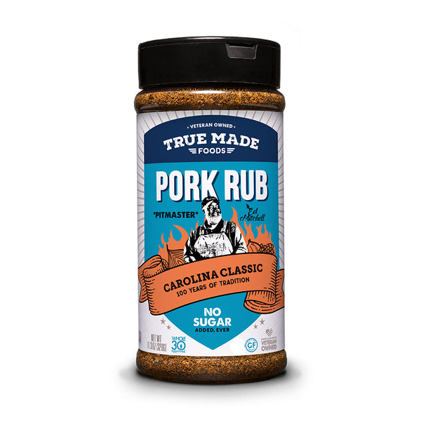 A bottle of True Made Foods Award Winning Pitmaster Pork Rub seasoning, Carolina Classic, on a clean white background. The bottle has a black cap and a label featuring a blue, white, and orange design with illustrations of barbecue smoke and a pig.